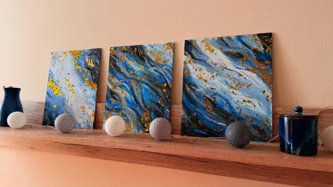 Triptych: Flow Three abstract acrylic paintings on canvas featuring a blue river stream motif and gold leaves, displayed on a wooden shelf.
